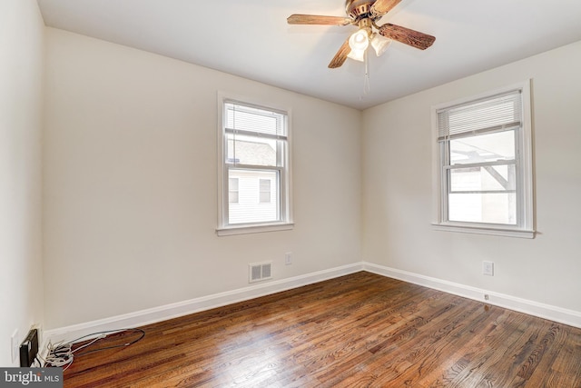 empty room featuring dark wood finished floors, visible vents, a ceiling fan, and baseboards