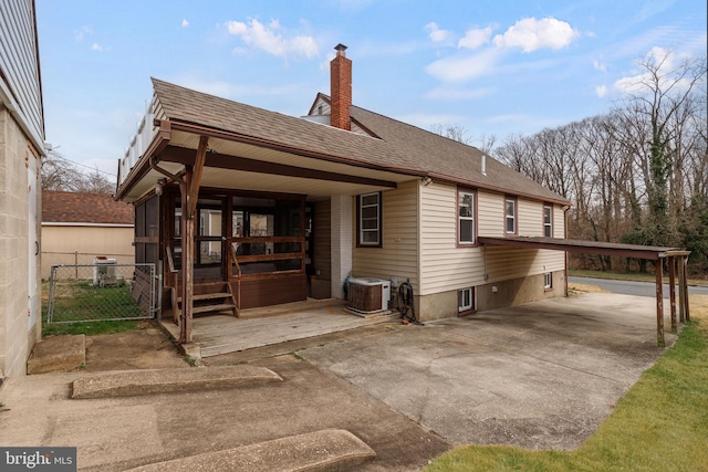 rear view of property with fence, central air condition unit, concrete driveway, roof with shingles, and a chimney