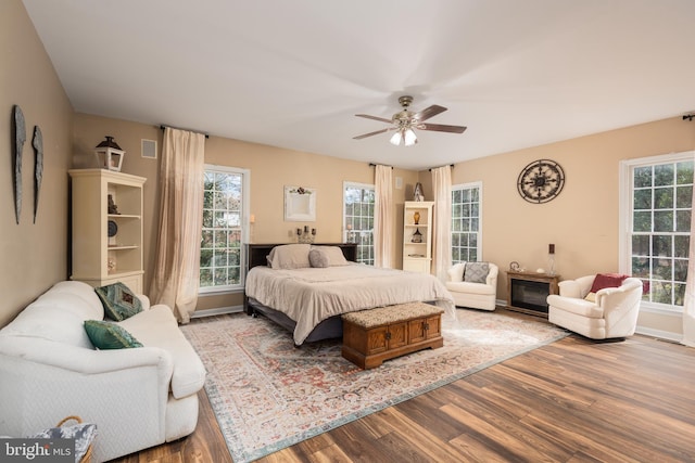bedroom featuring ceiling fan, baseboards, multiple windows, and wood finished floors