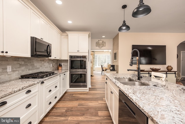 kitchen featuring backsplash, black appliances, wood finished floors, white cabinetry, and a sink