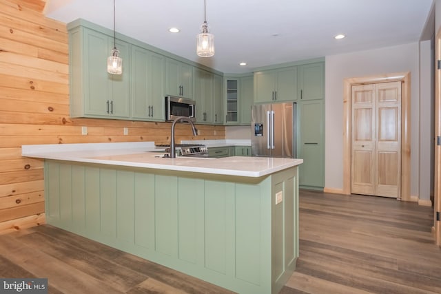 kitchen featuring stainless steel appliances, green cabinetry, a peninsula, light countertops, and dark wood-style flooring