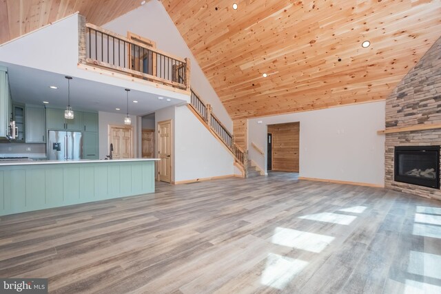 unfurnished living room with high vaulted ceiling, light wood-style floors, stairway, a stone fireplace, and a sink