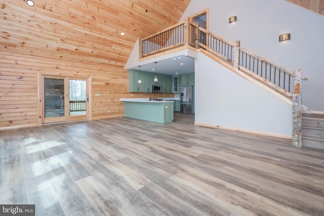 unfurnished living room featuring high vaulted ceiling, wood finished floors, wooden ceiling, stairs, and wooden walls