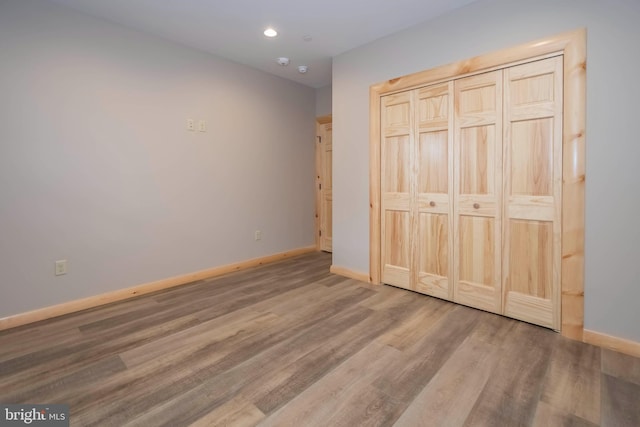 unfurnished bedroom featuring baseboards, wood finished floors, recessed lighting, and a closet