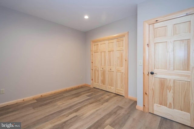unfurnished bedroom with wood finished floors, baseboards, recessed lighting, and a closet