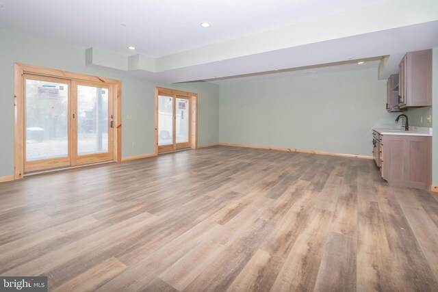 unfurnished living room featuring baseboards, light wood-type flooring, recessed lighting, and a sink