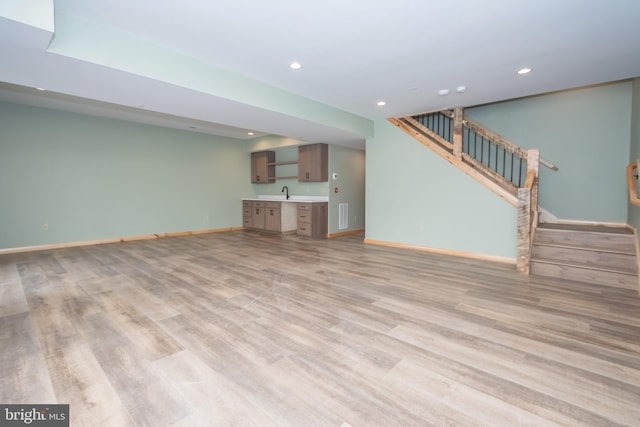 unfurnished living room featuring bar with sink, recessed lighting, stairway, light wood-style flooring, and baseboards