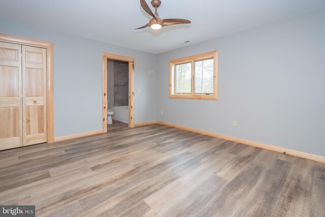 unfurnished bedroom with wood finished floors, baseboards, ensuite bathroom, a closet, and a ceiling fan