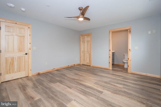 unfurnished bedroom with baseboards, wood finished floors, connected bathroom, and a ceiling fan