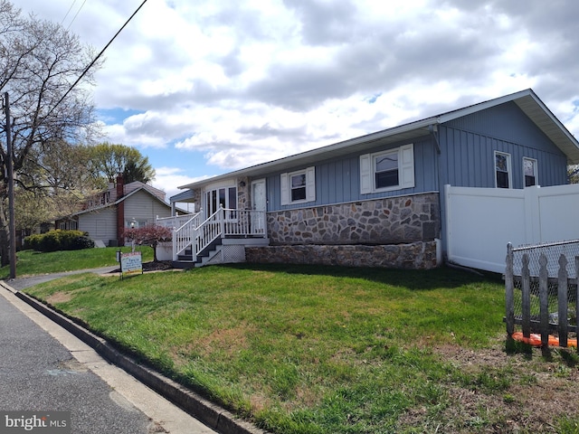 ranch-style home with a front lawn, fence, stone siding, and board and batten siding