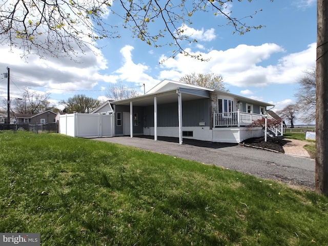 back of house with crawl space, aphalt driveway, a carport, fence, and a yard