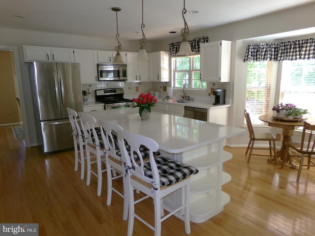 kitchen featuring light wood finished floors, a center island, a kitchen breakfast bar, white cabinetry, and appliances with stainless steel finishes