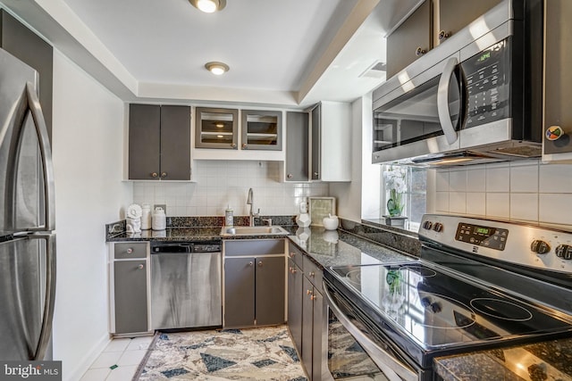 kitchen with backsplash, a sink, stainless steel appliances, and dark stone counters