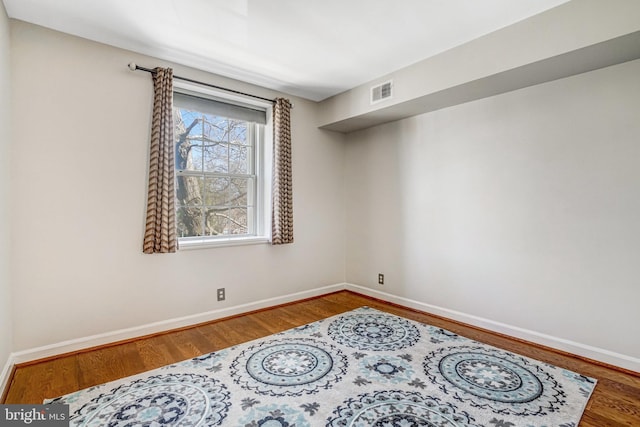 empty room with baseboards, visible vents, and wood finished floors