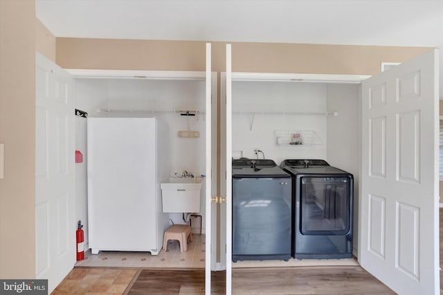 laundry area featuring laundry area, a sink, washer and clothes dryer, and wood finished floors