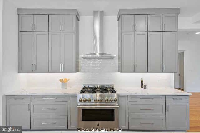 kitchen featuring high end stove, gray cabinets, light stone counters, and wall chimney range hood