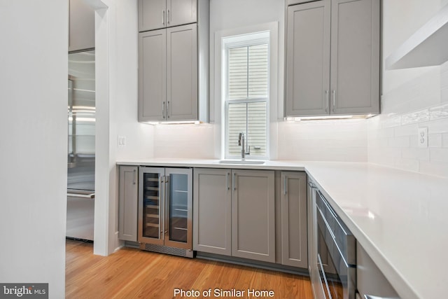 bar with a dry bar, tasteful backsplash, a sink, light wood finished floors, and beverage cooler