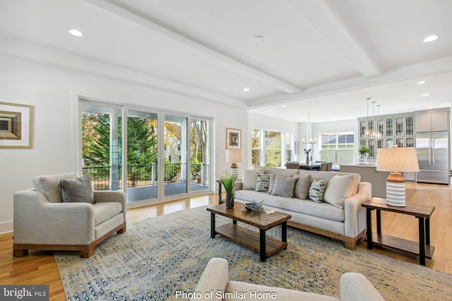 living area featuring light wood-style floors, a notable chandelier, a healthy amount of sunlight, and beamed ceiling