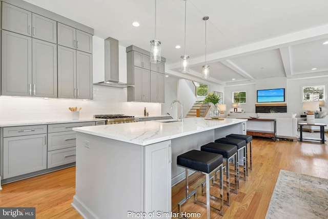 kitchen featuring a sink, wall chimney exhaust hood, light wood-type flooring, backsplash, and gray cabinetry