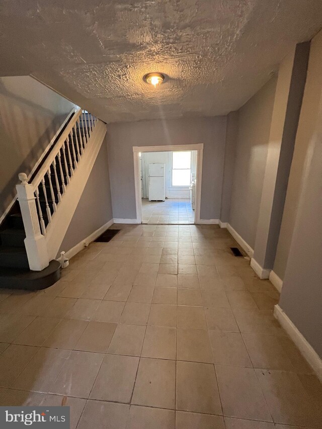 211 S Hilton St, Baltimore, MD 21229 - hall with tile patterned floors, stairway, a textured ceiling, and baseboards