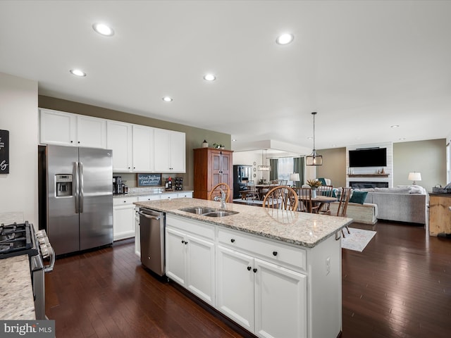 kitchen with a kitchen island with sink, a sink, appliances with stainless steel finishes, and dark wood-type flooring