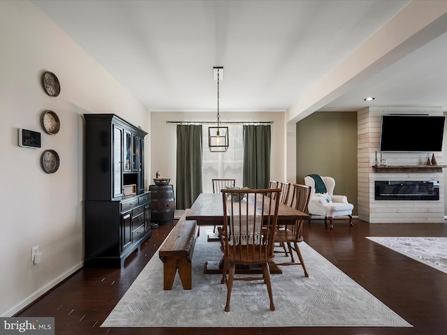 dining room featuring dark wood-type flooring, a fireplace, and baseboards