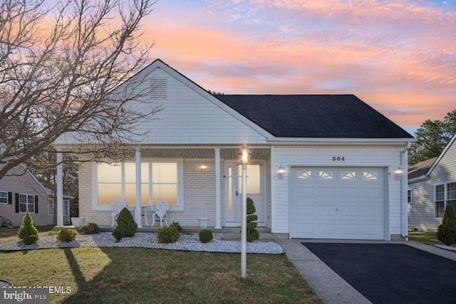view of front of house with a garage, a front yard, driveway, covered porch, and a shingled roof