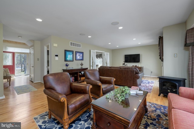 living room with a wood stove, light wood-style flooring, baseboards, visible vents, and recessed lighting