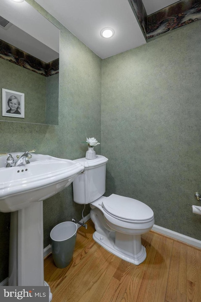 half bath with toilet, wood finished floors, visible vents, and a sink