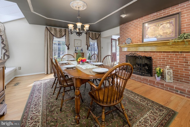 dining room with wood finished floors, a chandelier, a raised ceiling, baseboards, and a brick fireplace