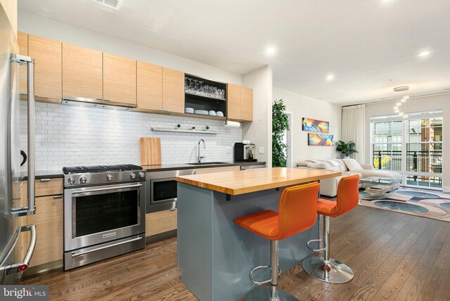 kitchen featuring a sink, dark wood-style floors, butcher block counters, under cabinet range hood, and stainless steel appliances