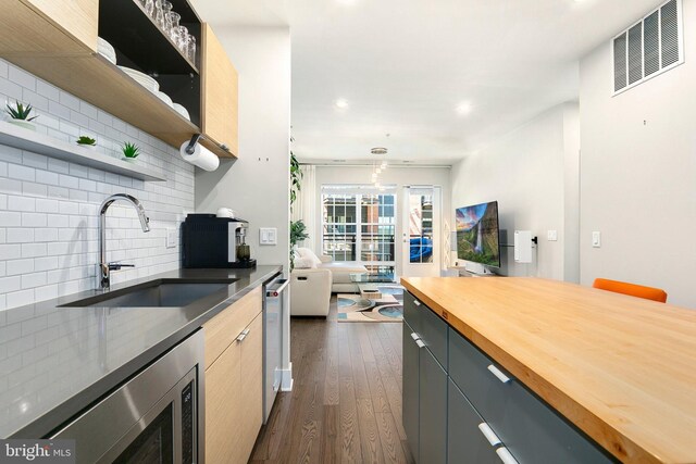 kitchen featuring a sink, stainless steel microwave, decorative backsplash, visible vents, and butcher block counters