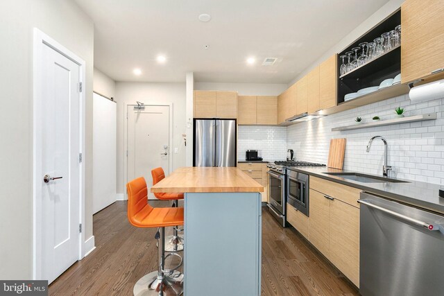 kitchen with a sink, a kitchen breakfast bar, butcher block countertops, stainless steel appliances, and backsplash
