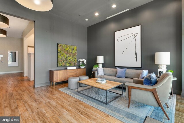 living room featuring recessed lighting, a high ceiling, baseboards, and light wood-type flooring