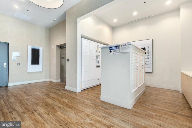 foyer entrance with baseboards, a high ceiling, light wood-type flooring, and elevator