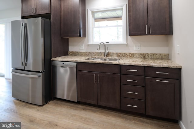 kitchen featuring light wood finished floors, light stone countertops, dark brown cabinets, appliances with stainless steel finishes, and a sink