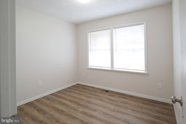 spare room with baseboards, visible vents, and wood finished floors