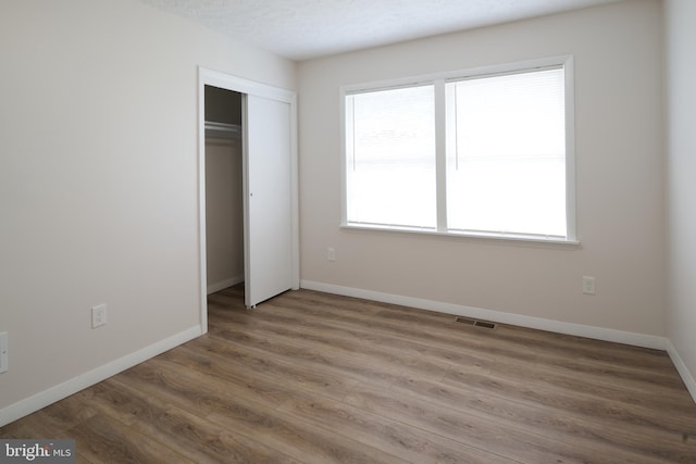 unfurnished bedroom with wood finished floors, a closet, baseboards, and visible vents