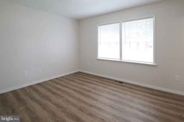 empty room with wood finished floors, baseboards, and visible vents