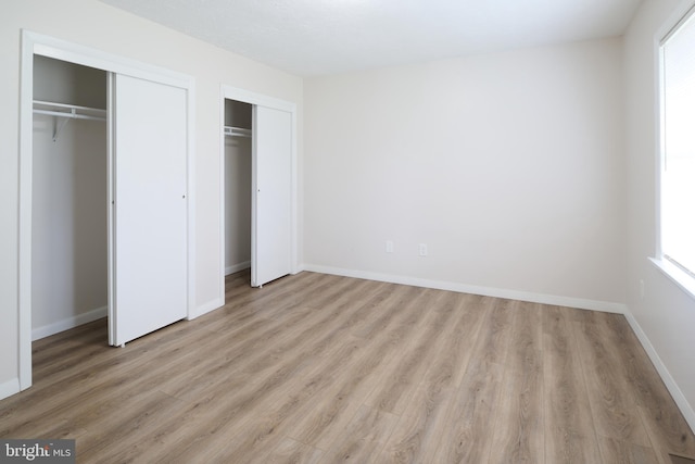 unfurnished bedroom with baseboards, wood finished floors, and two closets
