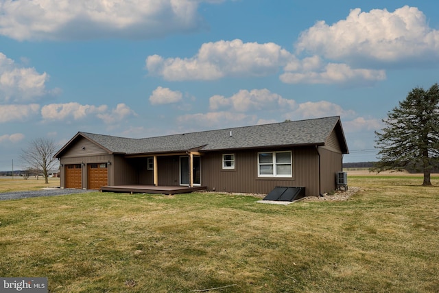 rear view of property featuring gravel driveway, a garage, a deck, a lawn, and cooling unit