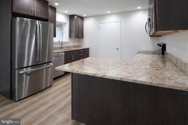 kitchen with light stone countertops, stainless steel appliances, dark brown cabinets, and a peninsula