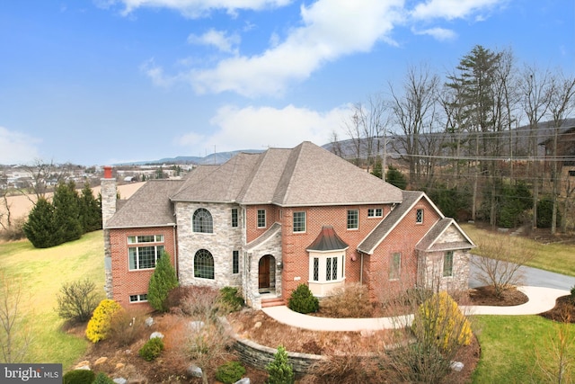 view of front of house featuring stone siding, a front yard, brick siding, a shingled roof, and a chimney