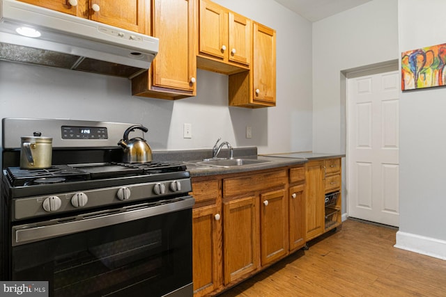2609 Keyworth Ave, Baltimore, MD 21215 - kitchen with light wood-type flooring, under cabinet range hood, gas stove, a sink, and dark countertops