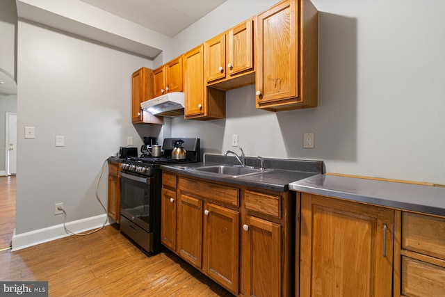 2609 Keyworth Ave, Baltimore, MD 21215 - kitchen featuring stainless steel gas range, dark countertops, under cabinet range hood, light wood finished floors, and a sink
