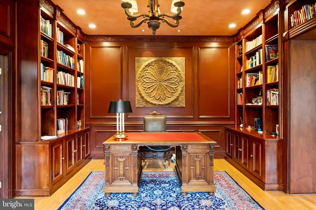 office featuring an inviting chandelier, a decorative wall, light wood-type flooring, and built in shelves