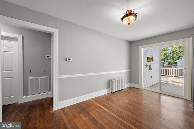 unfurnished room featuring visible vents, radiator heating unit, wood finished floors, and baseboards