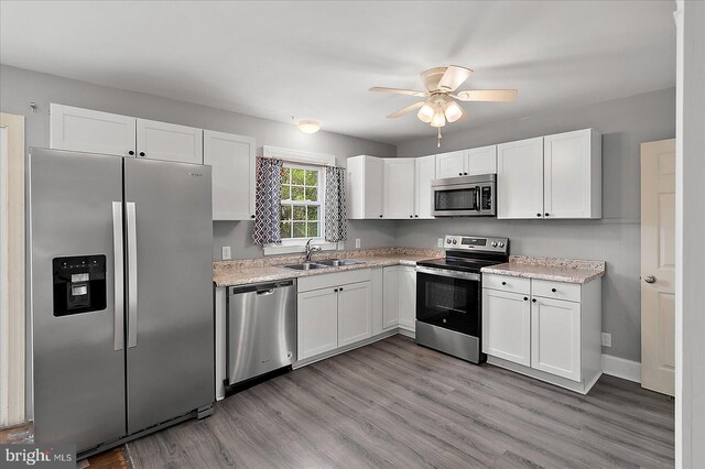 kitchen featuring light wood-style flooring, a sink, appliances with stainless steel finishes, and white cabinetry