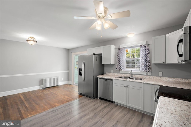 kitchen with appliances with stainless steel finishes, radiator, a sink, baseboards, and light wood-type flooring