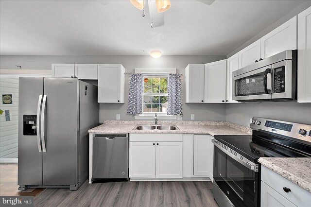 kitchen with wood finished floors, appliances with stainless steel finishes, a sink, white cabinetry, and a ceiling fan